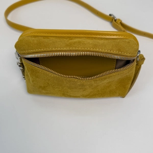 Detailed interior of mustard yellow suede crossbody bag with smooth lining and silver zipper