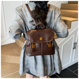 Detail of vintage brown PU leather backpack with gold twist lock on a white wall background