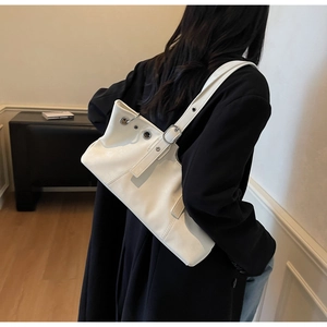 Detailed side view of white leather underarm bag with silver eyelets and adjustable strap