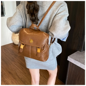 Close-up of vintage brown backpack with gold hardware worn by a model in a modern room