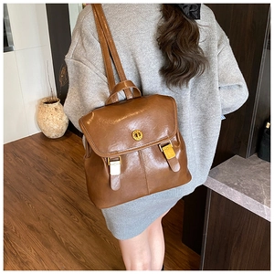 Detail of vintage brown PU leather backpack with gold metal clasp on a gray dress model