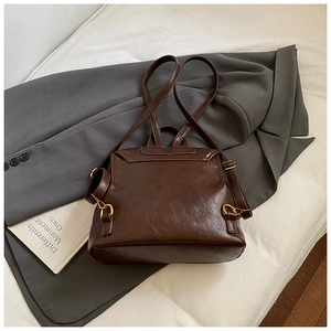 Detail of dark brown glossy PU backpack with gold hardware on a white bed sheet