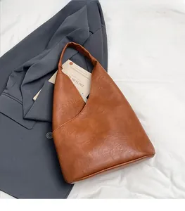 Detalle del bolso de hombro marrón con textura de cuero sobre un blazer gris elegante