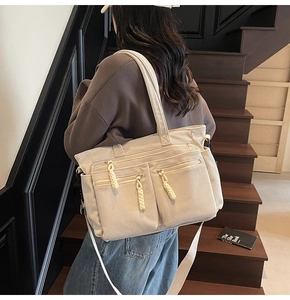 Detail of beige corduroy tote bag showing multiple zipper pockets and woven pull tabs