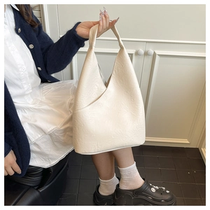 Primer plano del bolso tipo cubo en cuero crema texturizado con costuras en V únicas
