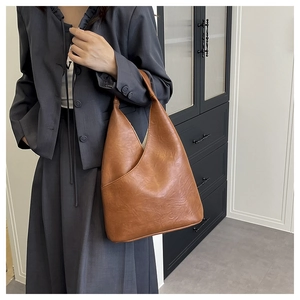 Bolso bucket de cuero marrón con diseño triangular lucido por modelo en traje