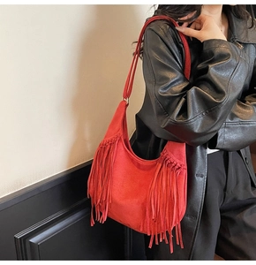 Détail du sac hobo rouge en daim avec franges porté sur un manteau en cuir noir