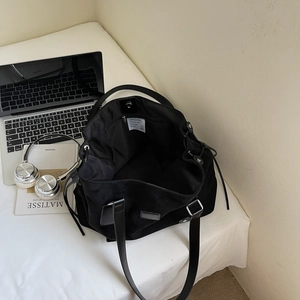 Large black matte tote bag with adjustable straps shown with laptop and headphones