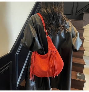 Sac hobo en daim rouge à franges porté par un mannequin en trench-coat en cuir noir