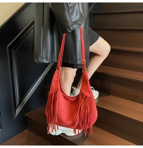 Détail du sac hobo en daim rouge avec de longues franges et une boucle dorée sur l'épaule