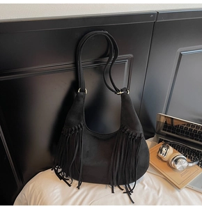Détail d'un sac hobo en daim noir avec franges et détails dorés dans un décor de bureau