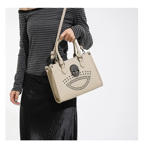 Close-up of beige tote bag featuring gothic skull stud details and smooth top handles