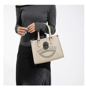 Detail of beige punk tote bag featuring black skull emblem and metal rivets decoration