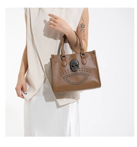 Brown tote bag with skull embellishment and rivets detail on light-colored outfit