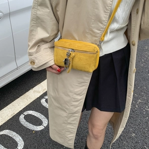 Yellow suede crossbody bag with robot charm shown on street background with beige trench coat
