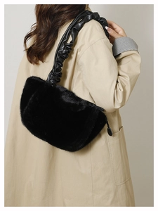 Detail of black faux fur shoulder bag with ruched leather handle on beige trench coat
