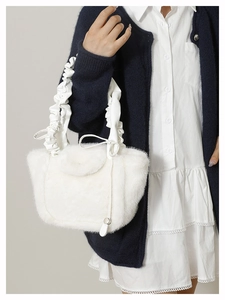 Detail of soft white faux fur handbag with a pleated leather strap and bow decoration