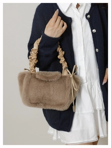 Detail of a brown plush shoulder bag with a light beige pleated handle and knot decor