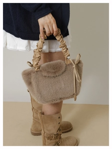 Detail of light brown faux fur handbag with a pleated handle and bow decoration
