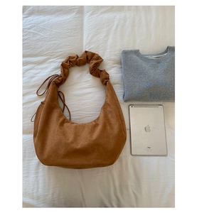 Detail view of brown suede dumpling bag with pleated handle and side drawstring