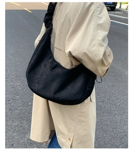 Side view of black suede large tote bag carried by a model in a beige trench coat