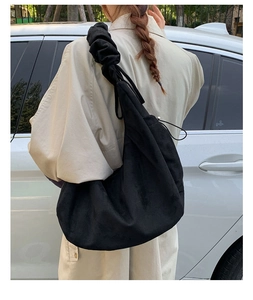 Detailed view of black suede drawstring tote bag with pleated shoulder strap design