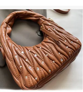 Detalle de bolso marrón plisado con pedrería brillante y material acolchado muy suave