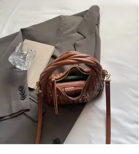 Detalle de bolso plisado matelassé marrón con asa trenzada y tachuelas metálicas