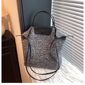 Close-up of black and white tweed bucket bag with leather handles and textured knit fabric