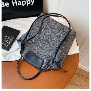 Top view of a grey tweed tote bag with black leather handles on a wooden table
