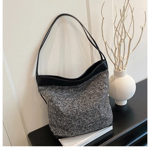 Detailed view of grey wool knit shoulder bag with black leather trim on a modern table