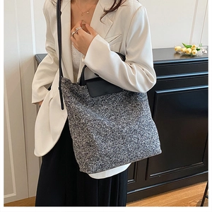 Detail of black and white tweed tote bag with leather flap handle shown on a model