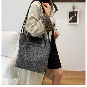 Detail of grey wool tote bag with black leather handle shown on model in minimal interior