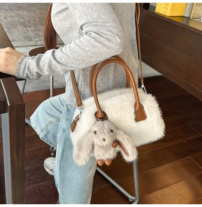 Dettaglio borsa in peluche bianca con manici in pelle marrone e ciondolo a coniglio