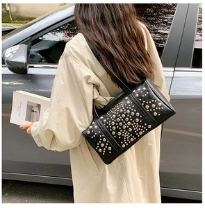 Detailed view of silver rivets on black leather shoulder bag worn by model outdoors