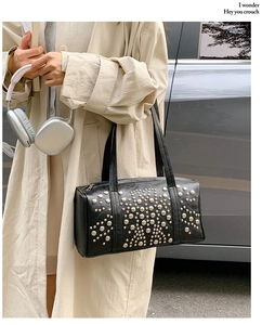 Close-up of black rivet cylinder bag with silver geometric patterns worn over the shoulder