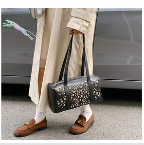 Close-up of black leather cylinder bag with silver stud patterns and dual top handles