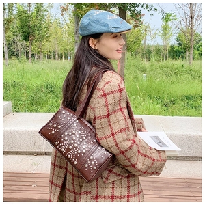 Detail of dark brown rivet studded shoulder bag styled with a checkered winter coat