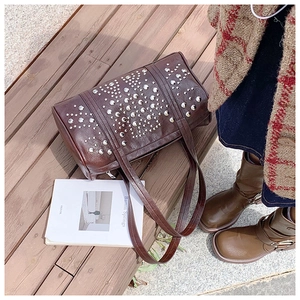 Detailed view of dark brown vintage Boston bag with silver rivets on a wooden bench