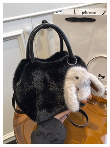 Detail of plush black handbag with white rabbit charm and leather shoulder strap