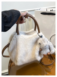 Detail of plush cream handbag with brown leather handles and cute rabbit charm