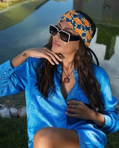 Detail van retro vierkante zonnebril met witte rand en een blauwe satijnen dames blouse
