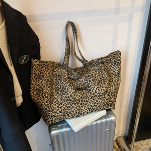 Large leopard print tote bag in brown and yellow tones styled on a silver suitcase