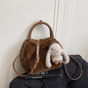 Brown faux fur handbag with leather handle and cute white bunny charm on a black cushion