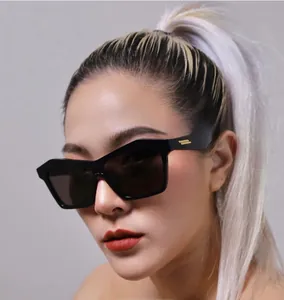 Detail shot of black cat-eye sunglasses featuring golden temple bars on a female model