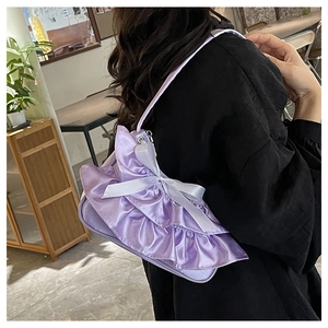 Detail of lavender ruffled tote bag with ribbon bow worn over a black top in a cafe