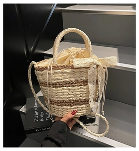 Detail of hand-woven straw bucket bag with lace bow and drawstring liner in hand