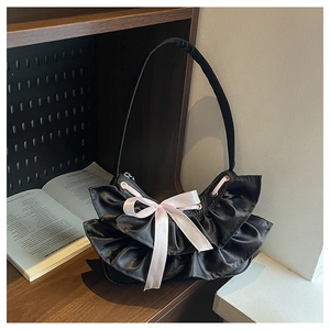 Detail of a black ruffled tote bag featuring a long pink satin bow on a wooden shelf