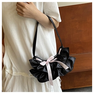 Detail of black ruffled shoulder bag with pink silk bow decoration on a warm background