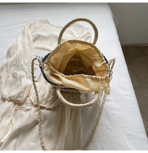 Detail view of woven straw bucket bag showing lace drawstring lining and dual handles